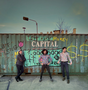 Bandfoto Acuario Cósmico: Drei Musiker vor bemaltem Container

Drei Personen stehen vor einem großen, türkisfarbenen Schiffscontainer mit Graffiti-Schriftzügen. Sie tragen gemusterte Hemden und dunkle Hosen. Der Hintergrund ist eine Industrieumgebung mit Betonboden und freiem Himmel.