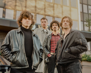 Bandfoto Soft Panic: Vierköpfige Band vor Gebäude

Vier Personen stehen vor einem modernen Gebäude mit großen Fenstern. Sie tragen Jacken und dunkle Kleidung. Die Kamera ist leicht von unten aufgenommen, wodurch die Gruppe geschlossen und kompakt wirkt.