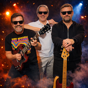Bandfoto New Breed: Drei Musiker mit Instrumenten
Drei Musiker posieren gemeinsam vor einem Hintergrund mit Bühnennebel und Lichteffekten. Zwei tragen Sonnenbrillen. Ein Musiker hält eine E-Gitarre, ein anderer einen Bass. Die Aufnahme wirkt wie ein klassisches Bandfoto.