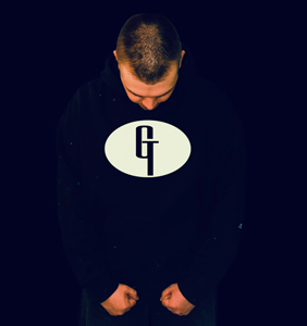 Bandfoto Good Trip: Musiker vor dunklem Hintergrund

Ein Musiker steht vor einem schwarzen Hintergrund und blickt nach unten. Er trägt einen dunklen Kapuzenpullover mit großem Logo auf der Vorderseite. Die reduzierte Beleuchtung lenkt den Fokus auf die Person und das Motiv auf dem Kleidungsstück.