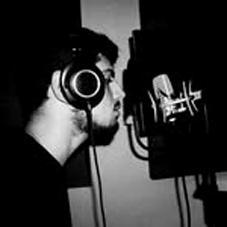 Bandfoto Slm Schwarz: Schwarzweiß-Aufnahme in einem Tonstudio. Ein Mann mit Kopfhörern steht vor einem Mikrofon, im Hintergrund sind Studioequipment und weitere Mikrofone zu erkennen. Die Szene zeigt den kreativen Aufnahmeprozess.