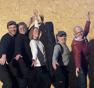 MoD (Bandfoto, 5 Personen)

Fünf Personen stehen dicht nebeneinander vor einer hellen Holzwand. Sie alle strecken lachend die Arme nach links oben. Von links nach rechts: ein Mann mit Kappe, eine Frau mit Locken und Brille, eine Frau mit glatten Haaren, ein Mann mit Mütze und Gitarrentasche auf dem Rücken, sowie eine Frau mit weißem Haar und roter Jacke.