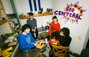Bandfoto Boo Central: Vierköpfige Band in einer Küche

Vier Musiker sitzen und stehen gemeinsam in einer kleinen Küche. Zwei Bandmitglieder halten Instrumente, darunter eine kleine Trommel und eine Gitarre. Im Hintergrund sind Küchenschränke, Arbeitsfläche und verschiedene Gegenstände zu sehen. An der Wand befindet sich der farbenfrohe Schriftzug „Boo Centraal“.