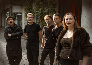 Bandfoto call me chris: Fünfköpfige Band im Freien

Fünf Musiker stehen gemeinsam auf einem gepflasterten Weg vor einem Gebäude. Vier Musiker tragen überwiegend schwarze Kleidung, die Musikerin im Vordergrund ein dunkles Oberteil und eine Jacke. Die Band blickt in die Kamera, im Hintergrund sind Hausfassade und Pflanzen zu sehen.