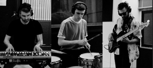 Band Foto Birdwatch:

Ein schwarz-weißes Foto in drei Abschnitten:
Links spielt ein Musiker an einem Keyboard, in der Mitte sitzt ein Schlagzeuger, rechts steht ein Bassist mit Sonnenbrille. Alle drei tragen Kopfhörer und wirken konzentriert. Die Szene spielt in einem Tonstudio, das Bild hat eine ruhige, dokumentarische Atmosphäre.