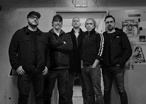 Band Foto Sinister Five:

Ein schwarz-weißes Gruppenfoto von fünf Männern in einem Proberaumflur.
Alle tragen dunkle Kleidung und blicken ernst in die Kamera. Im Hintergrund sind Poster und leicht abgenutzte Wände zu sehen, was dem Foto einen rohen, authentischen Charakter gibt.